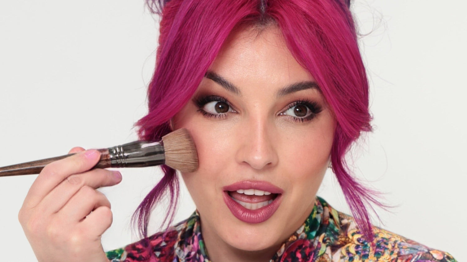 Person with colorful hair and clothing applying makeup with a brush on a white background